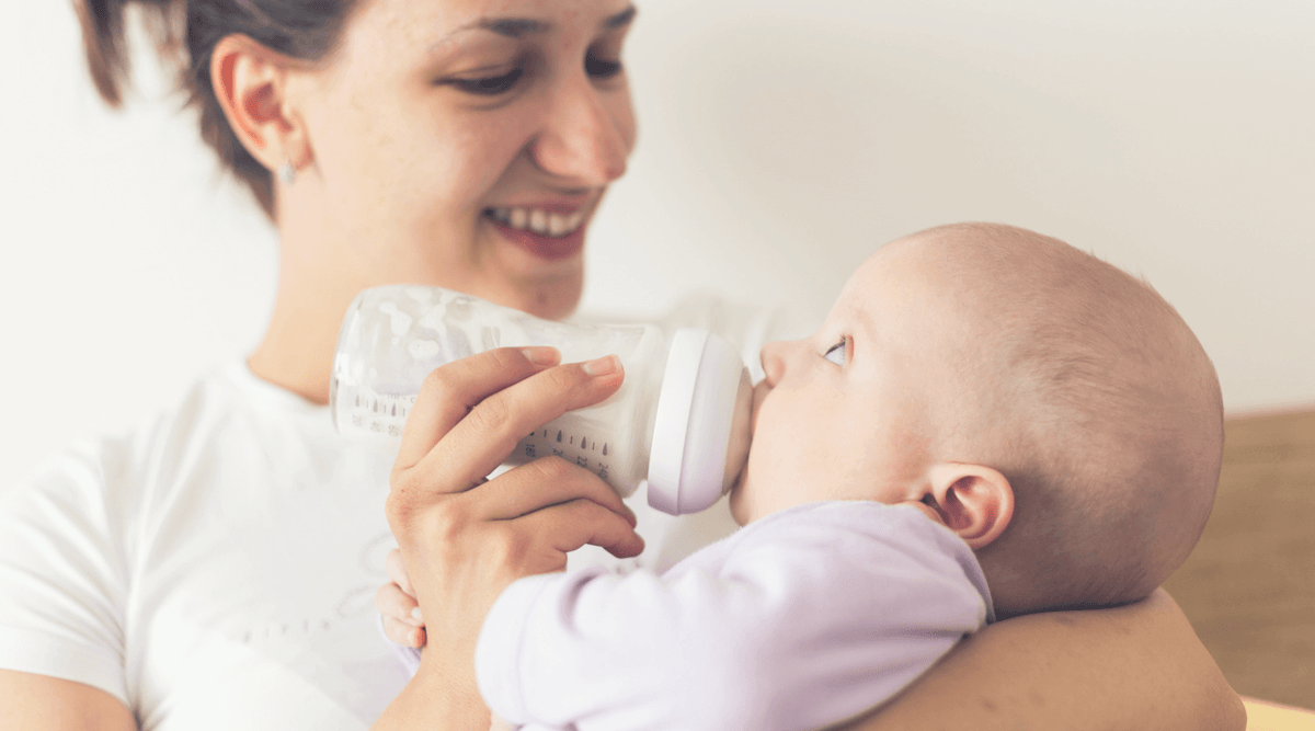 Mutter hält Baby im Arm und gibt Flasche mit Milch aus Flaschenwärmer